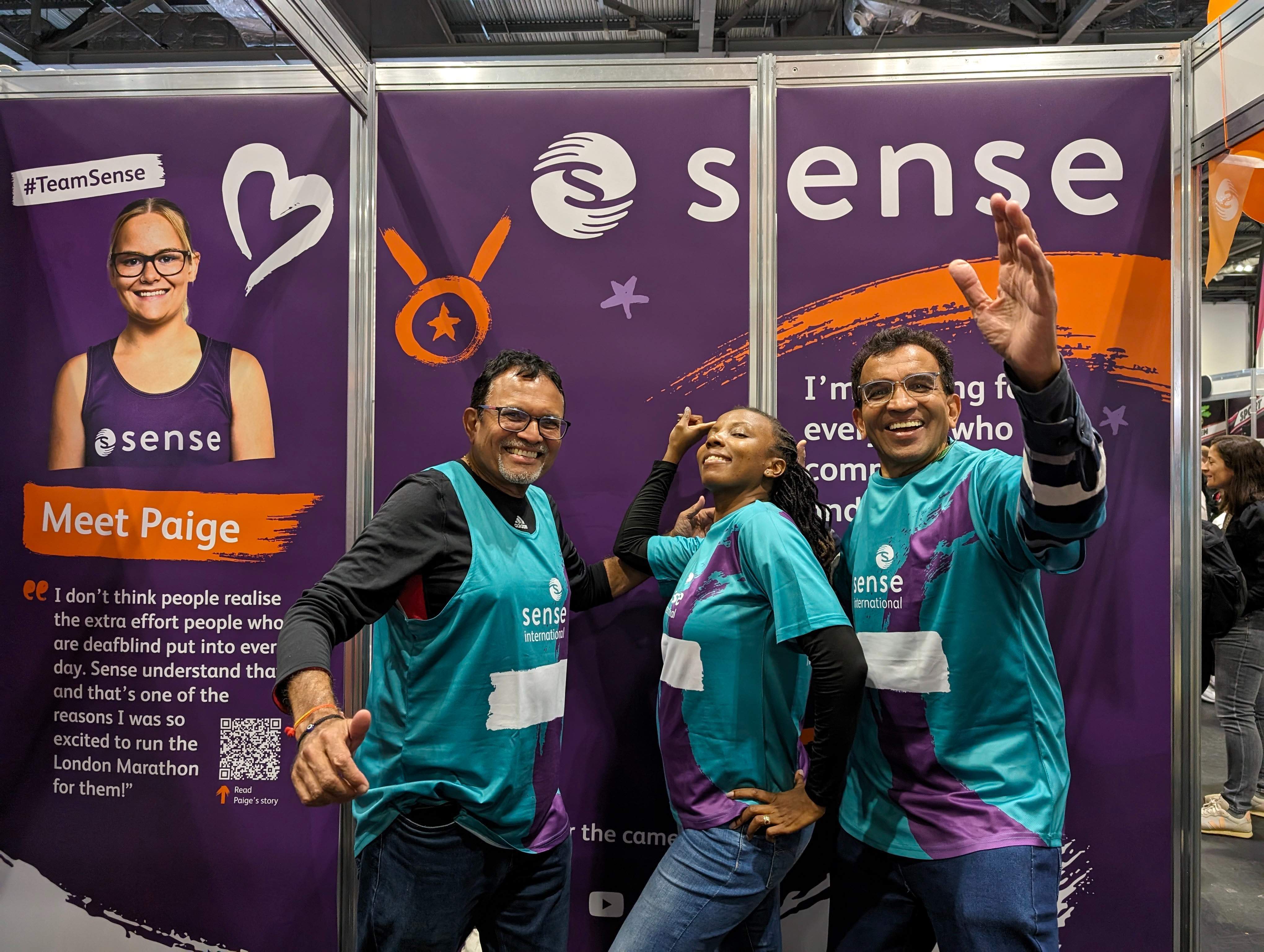 A group of runners stiking a pose in front of a Sense poster