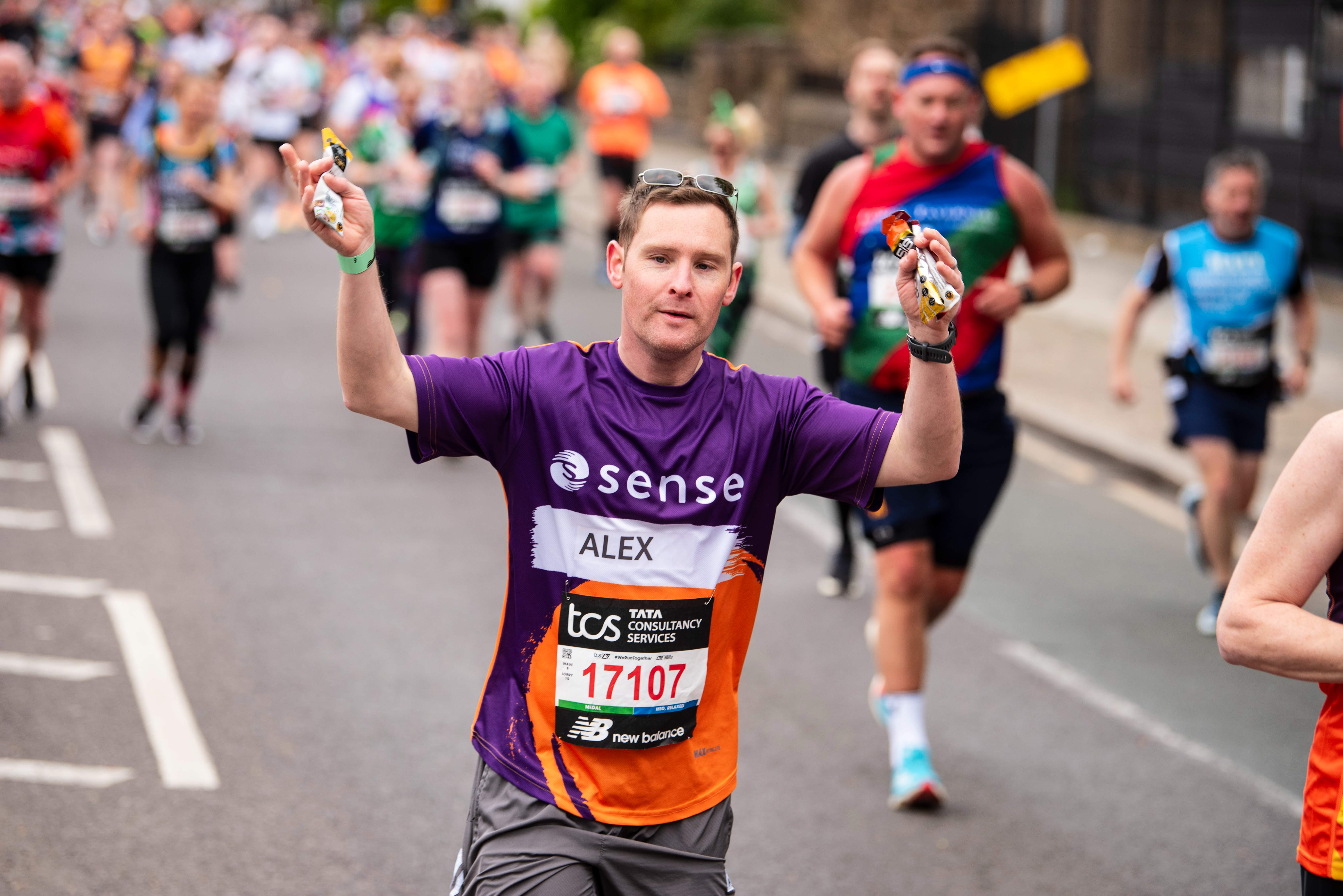 A man running with his arms in the air. He is wearing a Sense shirt.