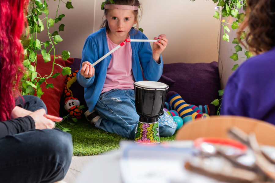 A young girl is holding up drum sticks as she plays a small wooden drum