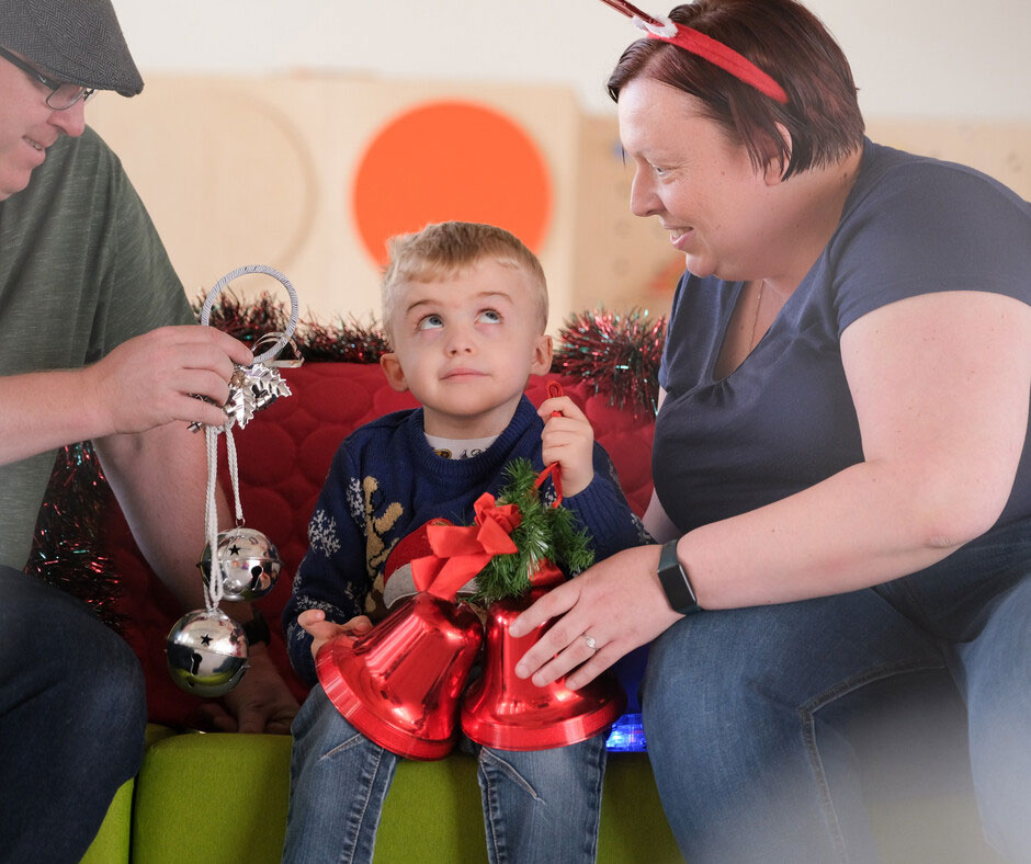 Thomas sits between his parents, gazing up at Mum. He's holding some Christmas decorations.