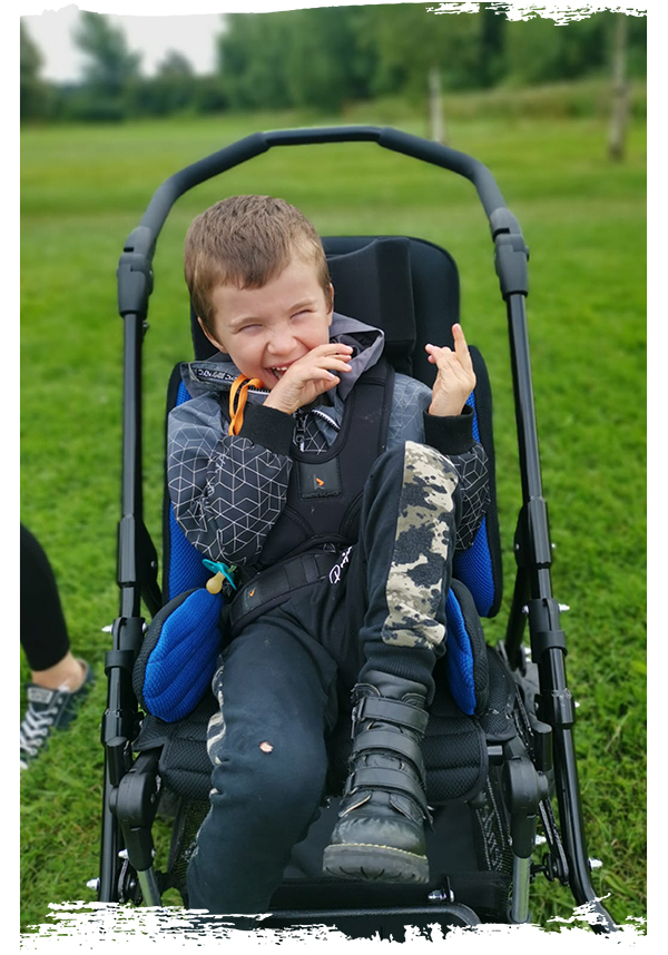 A boy is laughing in a pram on a grassy field