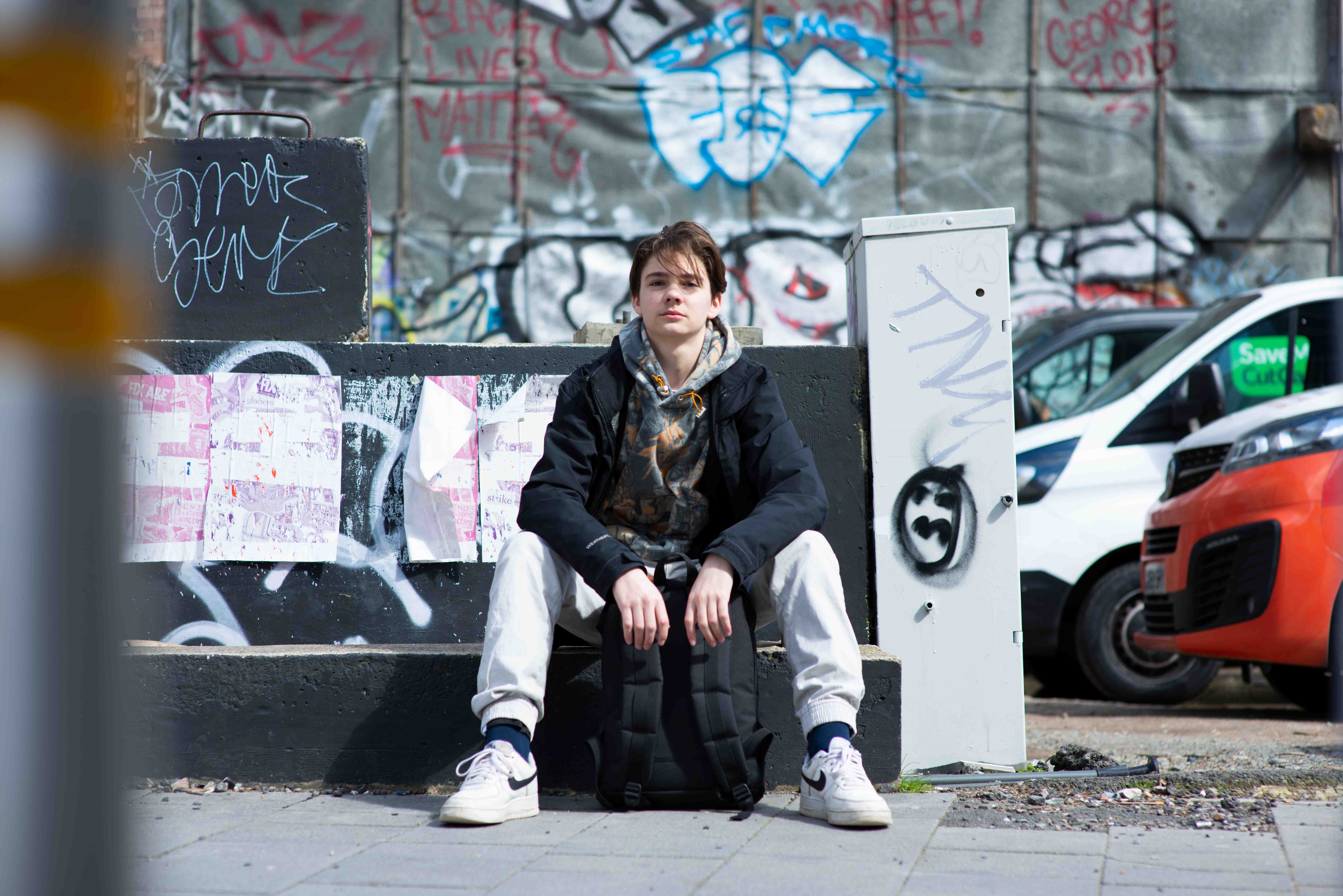 Young person sat in front of grafitti wall looking directly at camera