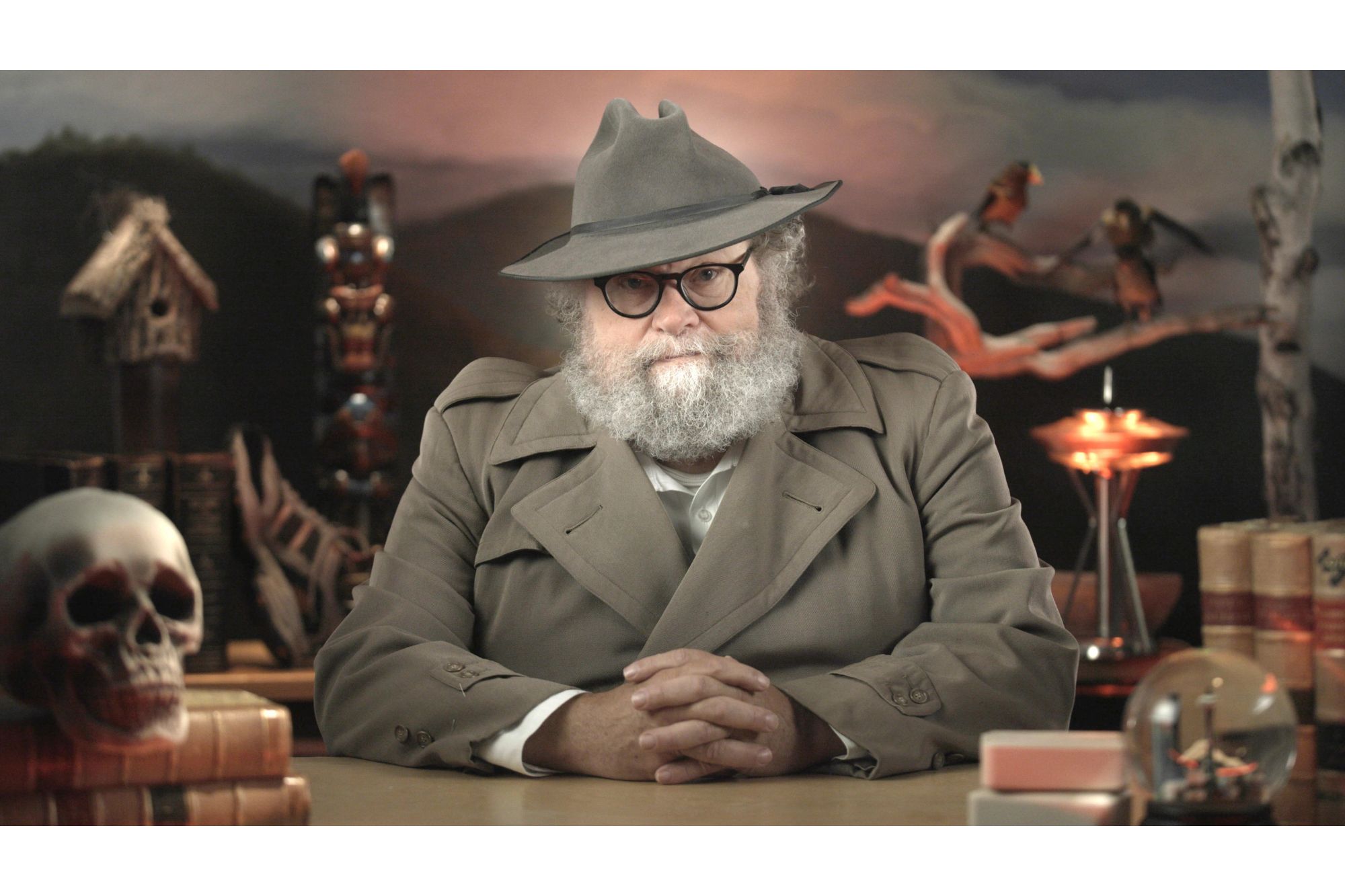 Knute Berger sits at a table wearing a detective-style coat and hat.