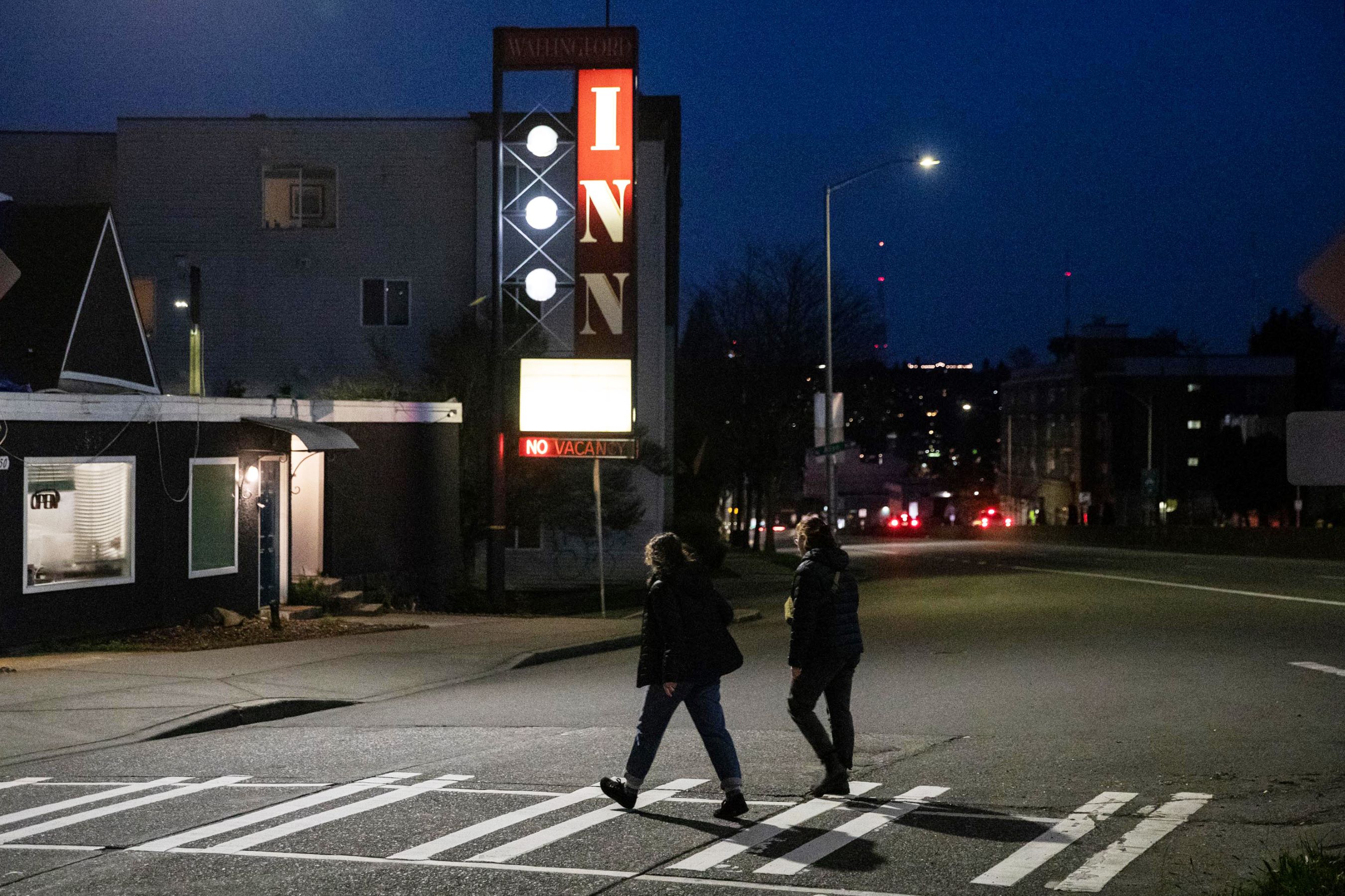 Two people cross Aurora Ave. in the dark.