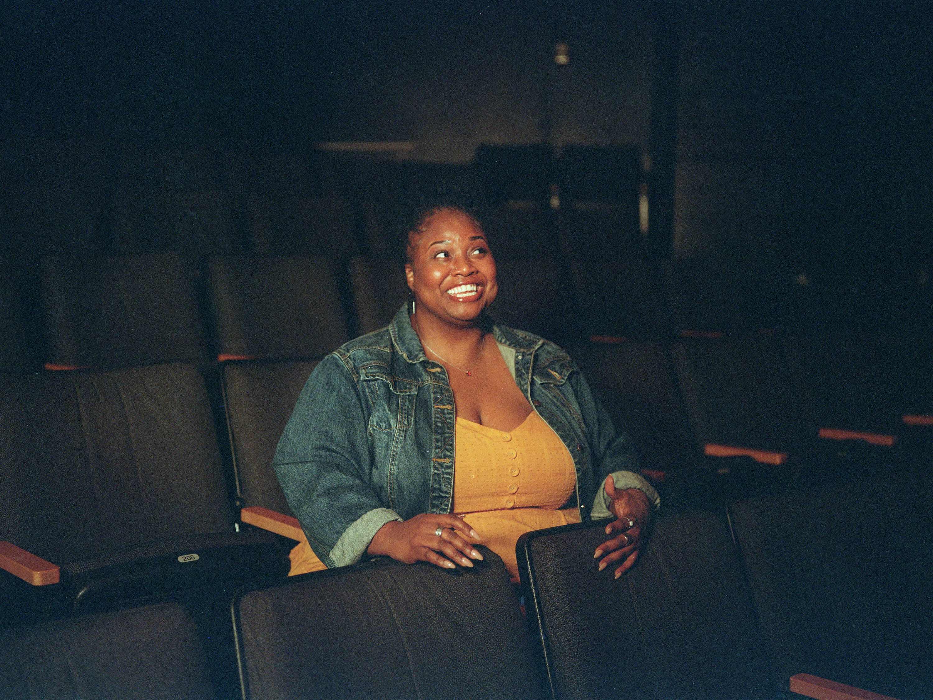 A woman sits alone in a theater, smiling broadly