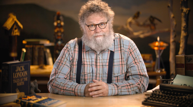 Knute Berger sits at a desk covered in books wearing a lumberjack flannel
