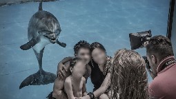 A family crouching down in front of a glass tank, having their photo taken, as a dolphin swims behind them