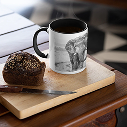 A mug with black and white elephant photo on it, next to a piece of cake