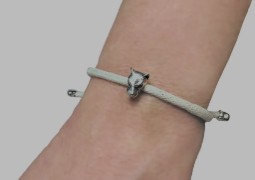 A woman's wrist wearing a while cord bracelet with a silver lioness head attached.