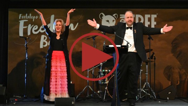 A photo of Dame Joanna Lumley and James Lewis with their arms outstretched on stage at the Born Free Ball - click to watch video