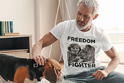 A grey-haired man wearing a white 'freedom fighter' T-shirt , stroking a beagle