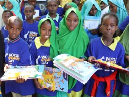 A photo of a group of young Kenyan school children wearing brightly coloured Giraffe Day T-shirts, holding activity books