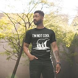 A man walking through a park with his hand in hos pocket, wearing a black T-shirt which says 'I'm not cool' and features a stylised drawing of a polar bear.