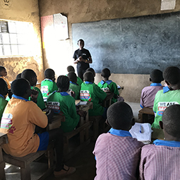Primary school children in Kenya facing a teacher in front of a blackboard