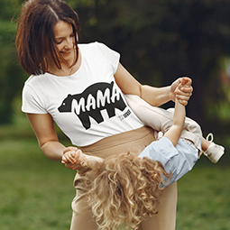 A woman in a white tshirt with 'mama' and a bear on it, swinging a young child