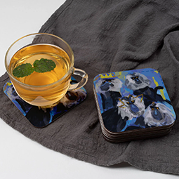 A mug on a coaster next to a stack of coasters with painted mandrills on