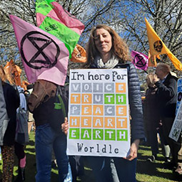 Dr Nikki Tag holding a poster at a protest, with people carrying brightly coloured flags in the background