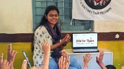 A photo of Shivangi Bendre in a classroom with raised childrens' hands in the foreground.