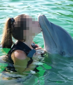 A photo of a woman kissing a dolphin on the nose, in a swimming pool