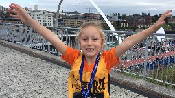 A young girl with her arms outstretched, wearing a Born Free running vest and medal