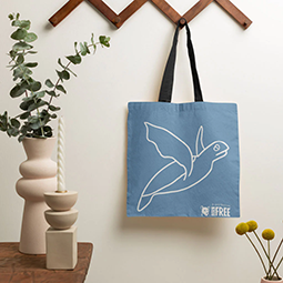 A blue tote bag with a white turtle motif hanging on the wall